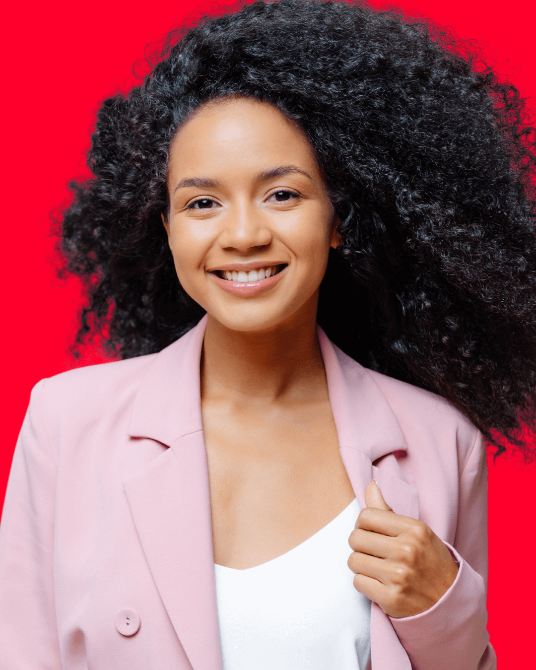 Woman with black curly hair wearing light pink jacket smiling.