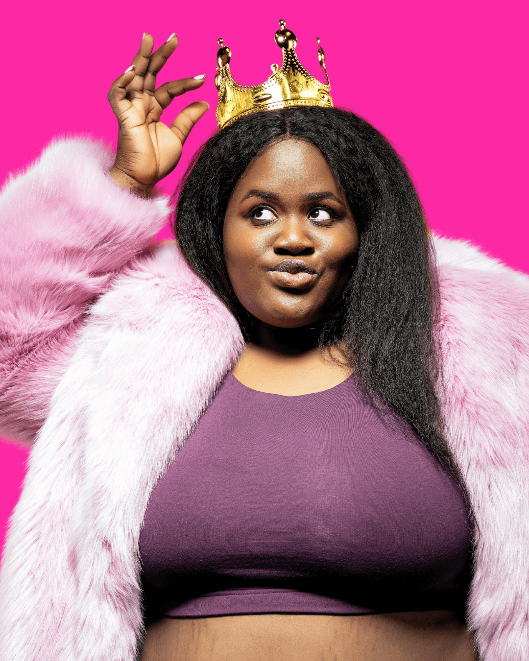Woman in fluffy pink jacket holding a gold crown on her head.